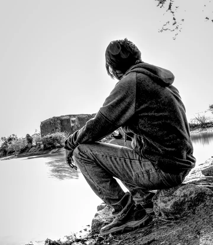 Gerard Reyes de espaldas, en cuclillas frente a un cuerpo de agua en blanco y negro: una imagen para mirar el mundo desde su perspectiva, no para mirarlo a él.